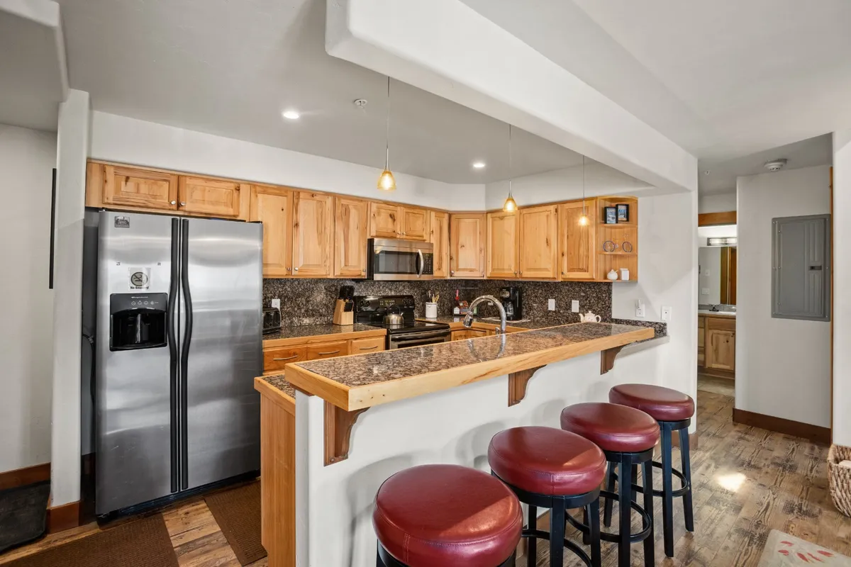 This image features a modern kitchen with a spacious island, bar stools, stainless steel appliances, and warm wooden cabinetry. The setting feels inviting and is ready for casual dining or socializing, evoking a sense of home base for guests exploring the town.