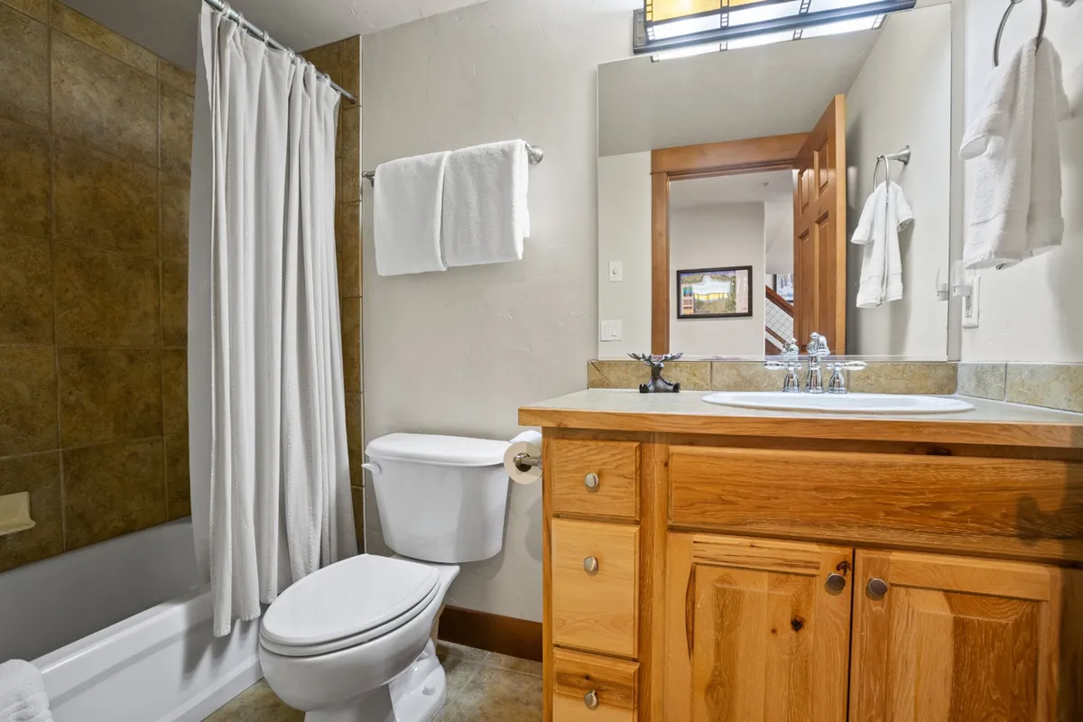 A clean, refreshing bathroom with a vanity, sink, toilet, bathtub, and a simple shower curtain. The space is bright and calming, perfect for unwinding after a day outdoors or preparing for another adventure.