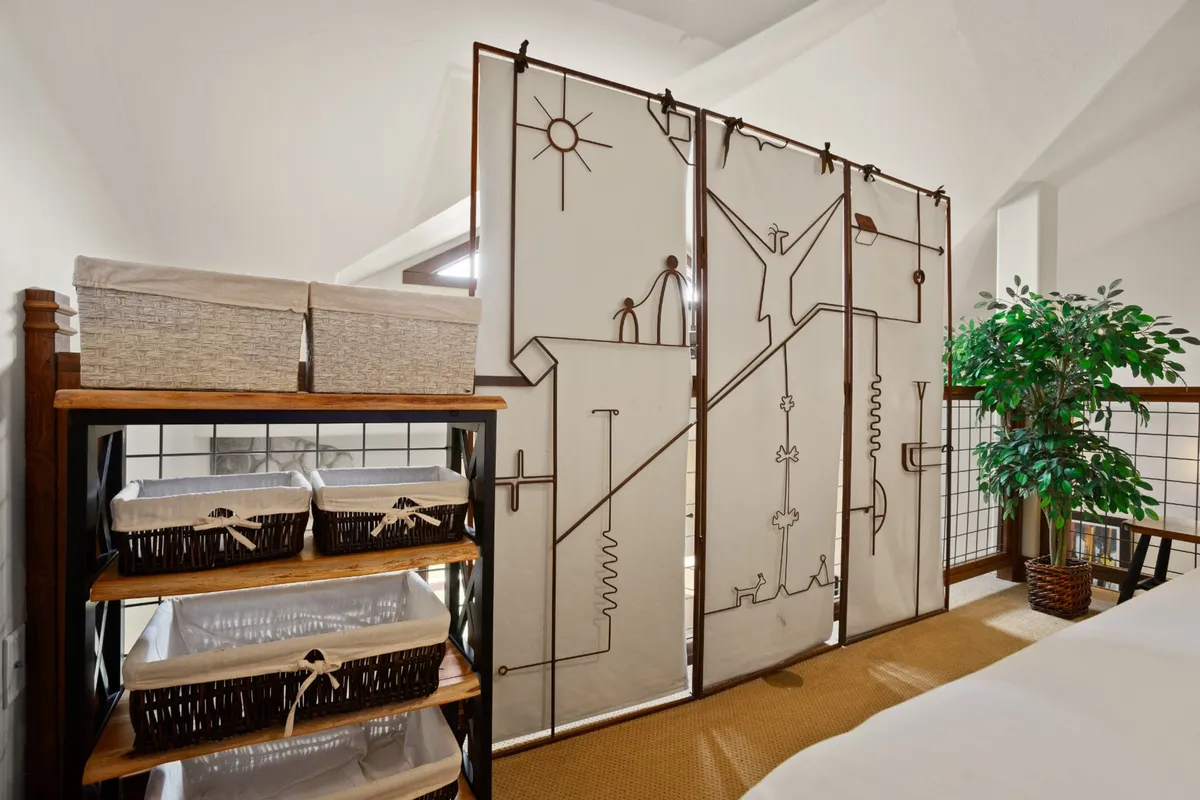 This image features a decorative room divider, storage baskets, and an indoor plant, with soft light filtering in from a window. The divider hints at flexible room arrangements and privacy options, while the tranquil decor evokes a comfortable, homey feel.