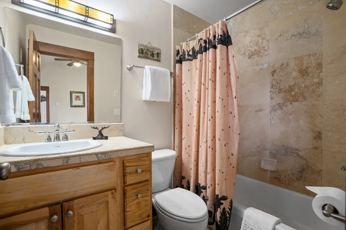 A well-lit bathroom featuring wooden cabinetry, a mirrored vanity, and a shower curtain with a nature motif. The space exudes tranquility and offers both function and style for group stays.