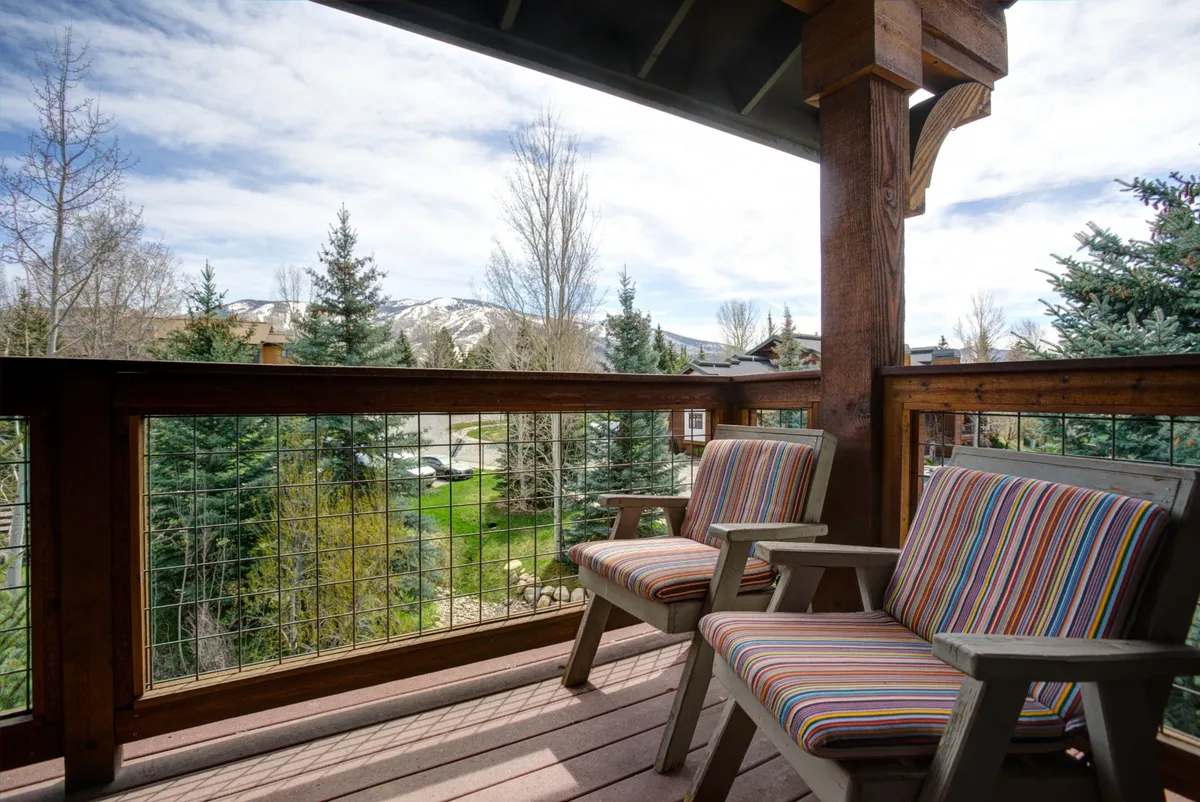 A covered balcony furnished with striped chairs and a wooden railing, overlooking breathtaking mountain views. The setting is inviting for relaxing, socializing, or simply soaking in the alpine scenery.